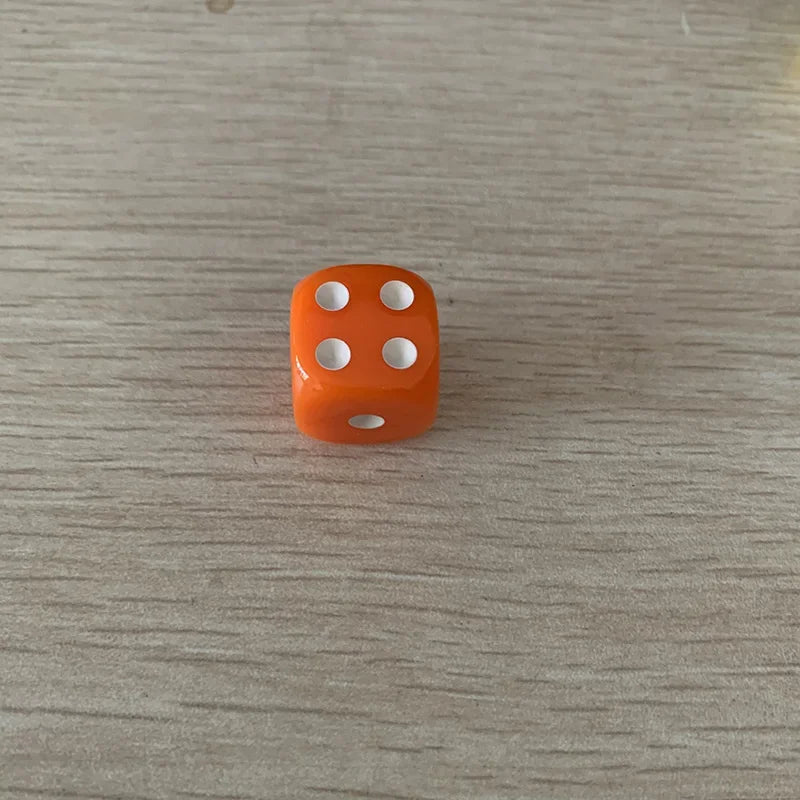 A single orange acrylic die with five white dots is placed on a light wooden surface.