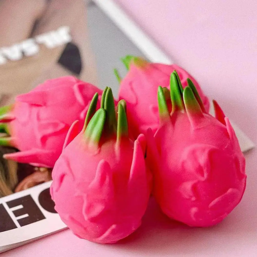 A close-up of a bright pink dragon fruit squishy stress relief toy resting on a light surface.