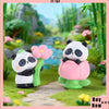 A cute panda collectible figure in white and black with pink flowers standing on a green landscape.