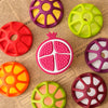 A collection of silicone baby teethers shaped like various fruits and vegetables in bright colors on a piece of paper.