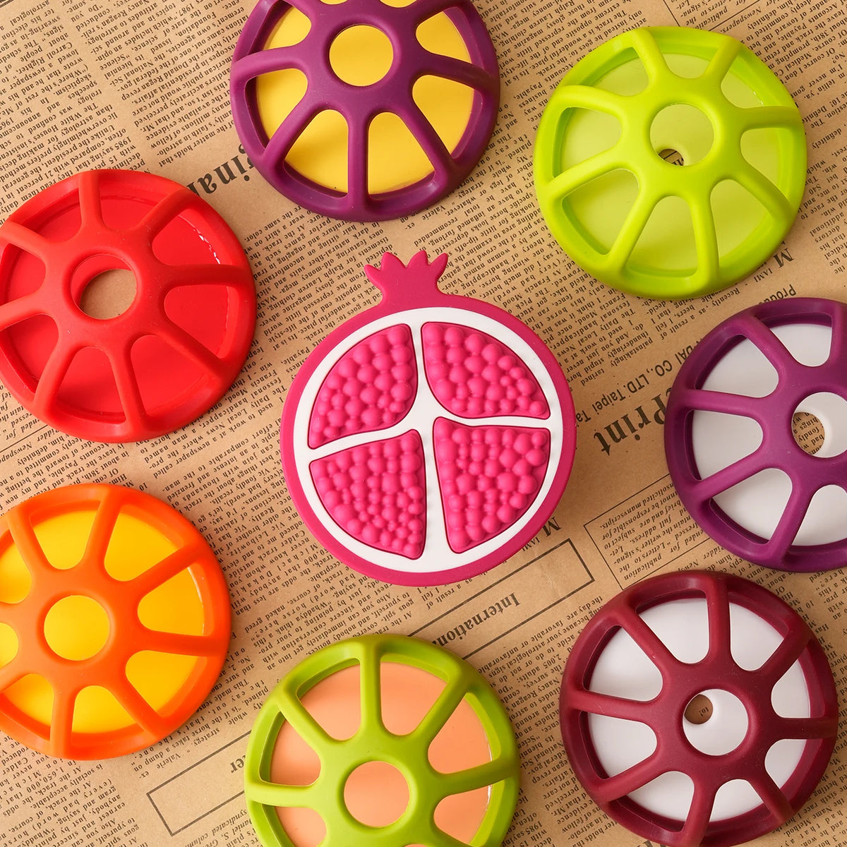 A collection of silicone baby teethers shaped like various fruits and vegetables in bright colors on a piece of paper.