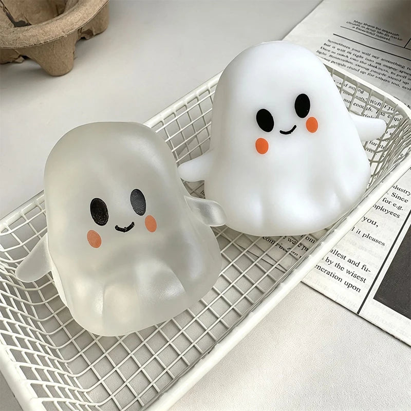 A pair of white, squishy ghost-shaped silicone toys with black eyes and orange accents resting in a white mesh tray.