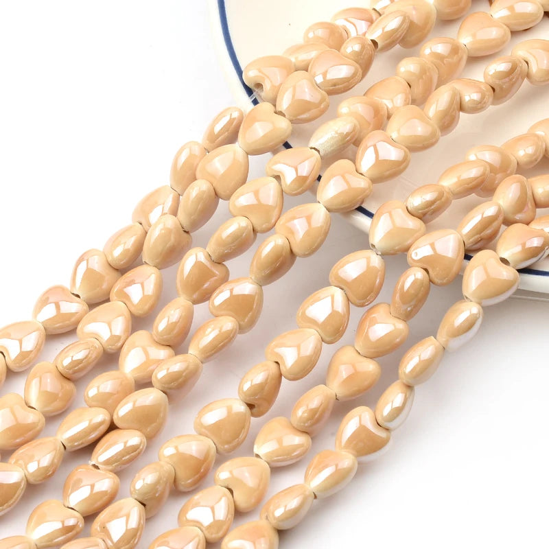A close-up of multiple strands of light beige and white heart-shaped acrylic beads for jewelry making.