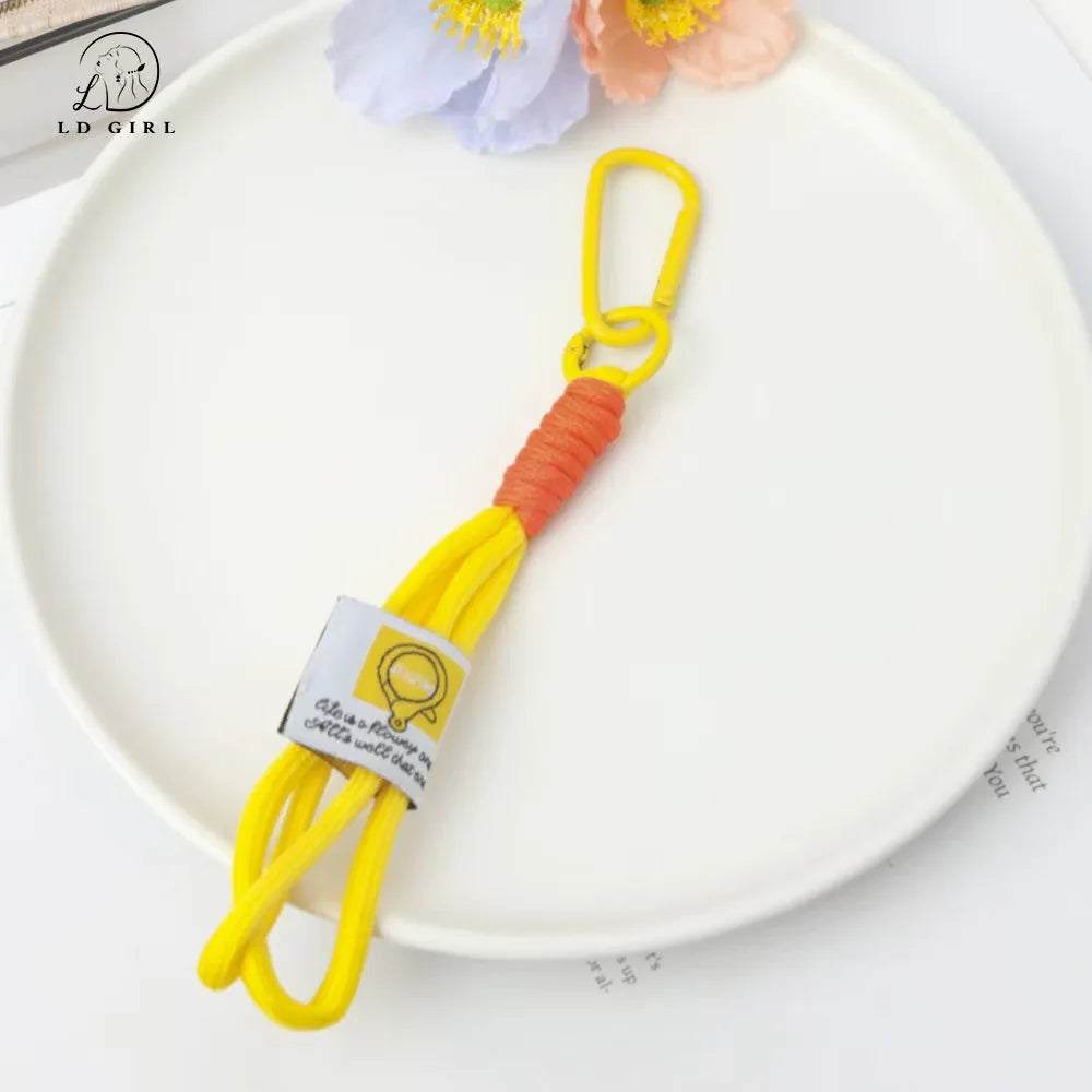 Yellow soft bunny plush keychain with an orange cord and bow charm resting on a white plate.