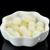 A white bowl filled with small, round, light yellow pearl beads for jewelry making.