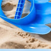A bright blue dinosaur claw sand digging toy is shown scooping sand in a sandy environment.