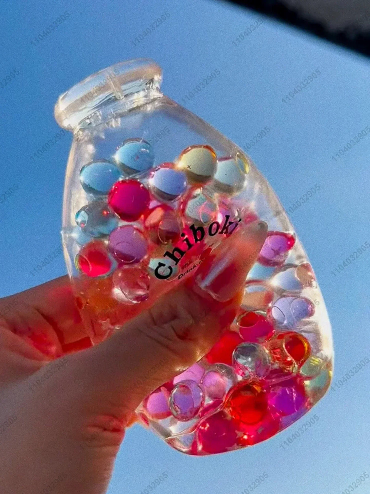 A hand holds a clear bottle filled with colorful, squishy fruit-shaped stress balls.