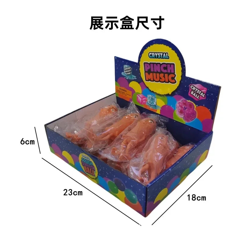A box containing a crystal pinch music toy with orange-colored plastic pieces, shown from above.