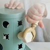 A child's hand is shown interacting with a green Montessori screwdriver board toy for fine motor skills and shape matching.