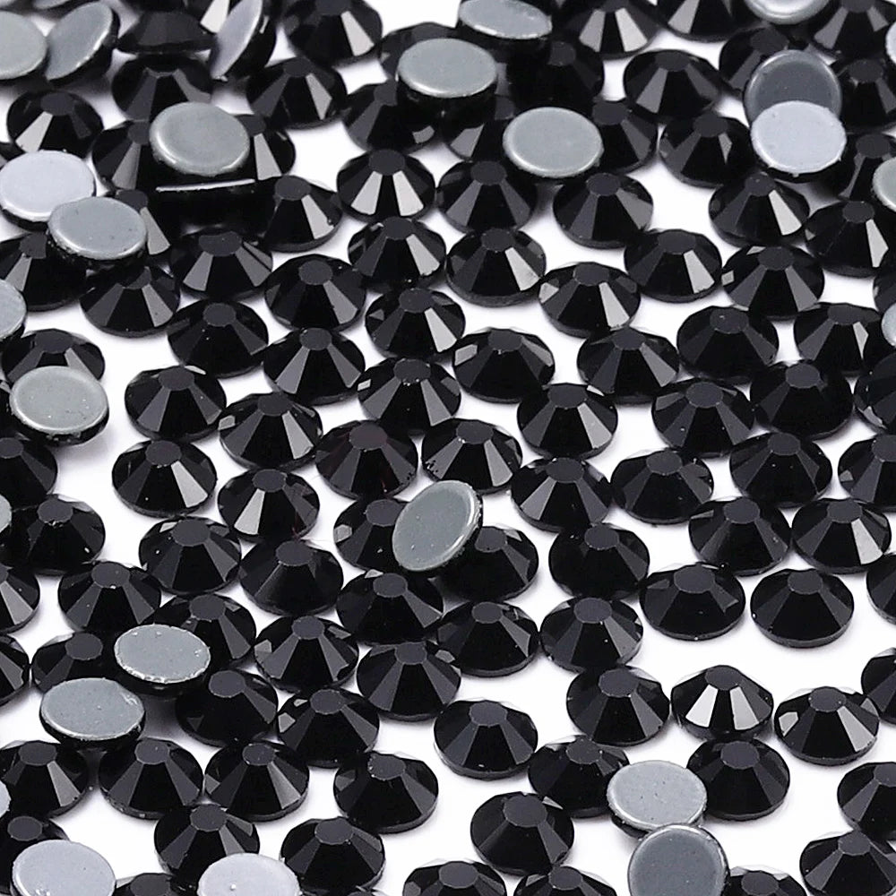A close-up view of small, round black glass crystal hot fix rhinestones scattered on a white background.