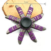 A metal fidget spinner with a star shape and purple braided string detail resting on a wooden surface.