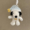 A white dog plush toy resembling Snoopy wearing a light blue hat and a yellow flower, attached to a keychain.