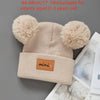 A beige knit baby beanie hat with fluffy pom-poms, suitable for infants aged 0-3 years old.