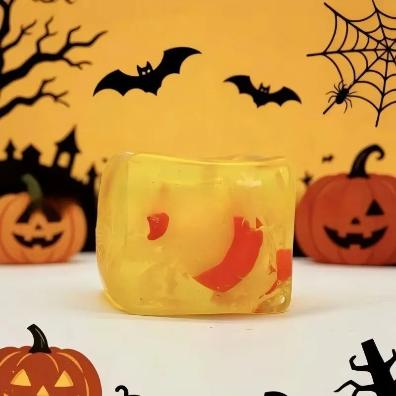 A yellow squishy ice cube toy shaped like a Halloween ghost dumpling, set against a background of bats and spiders.