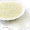 A close-up view of small, glossy, pale yellow glass seed beads scattered on a white surface.