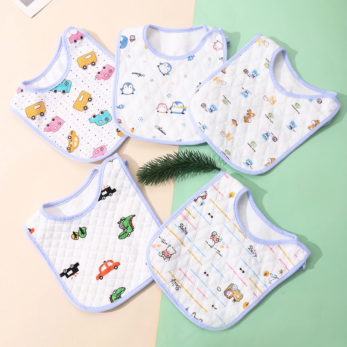 A set of three white cotton baby bibs with various colorful embroidered patterns and adjustable closures arranged on a light 