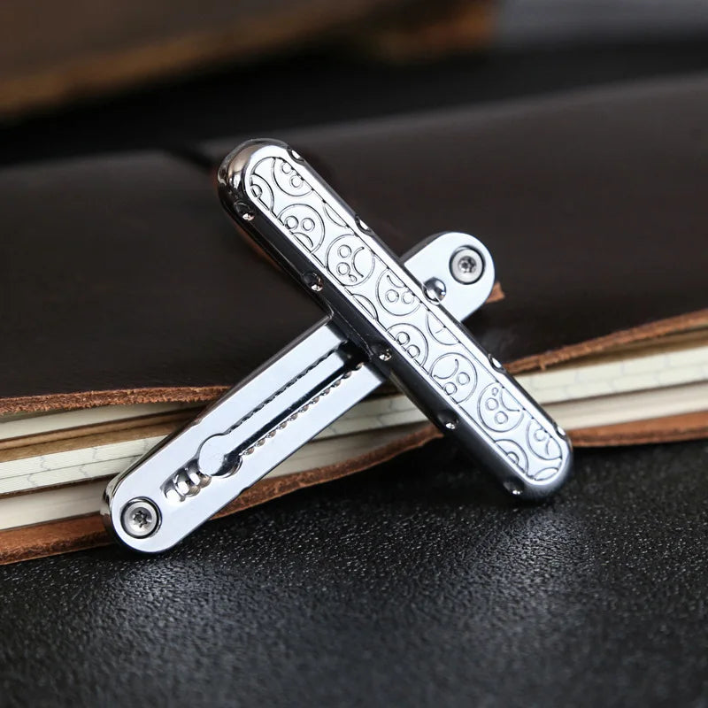 A silver metal fidget slider tool is shown crossed on a dark surface next to a leather-bound notebook.