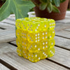 A stack of 36 transparent yellow dice in a clear display case resting on a wooden surface.