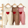 Three pairs of toddler corduroy overalls in cream, brown, and pink hanging on a wooden rack.
