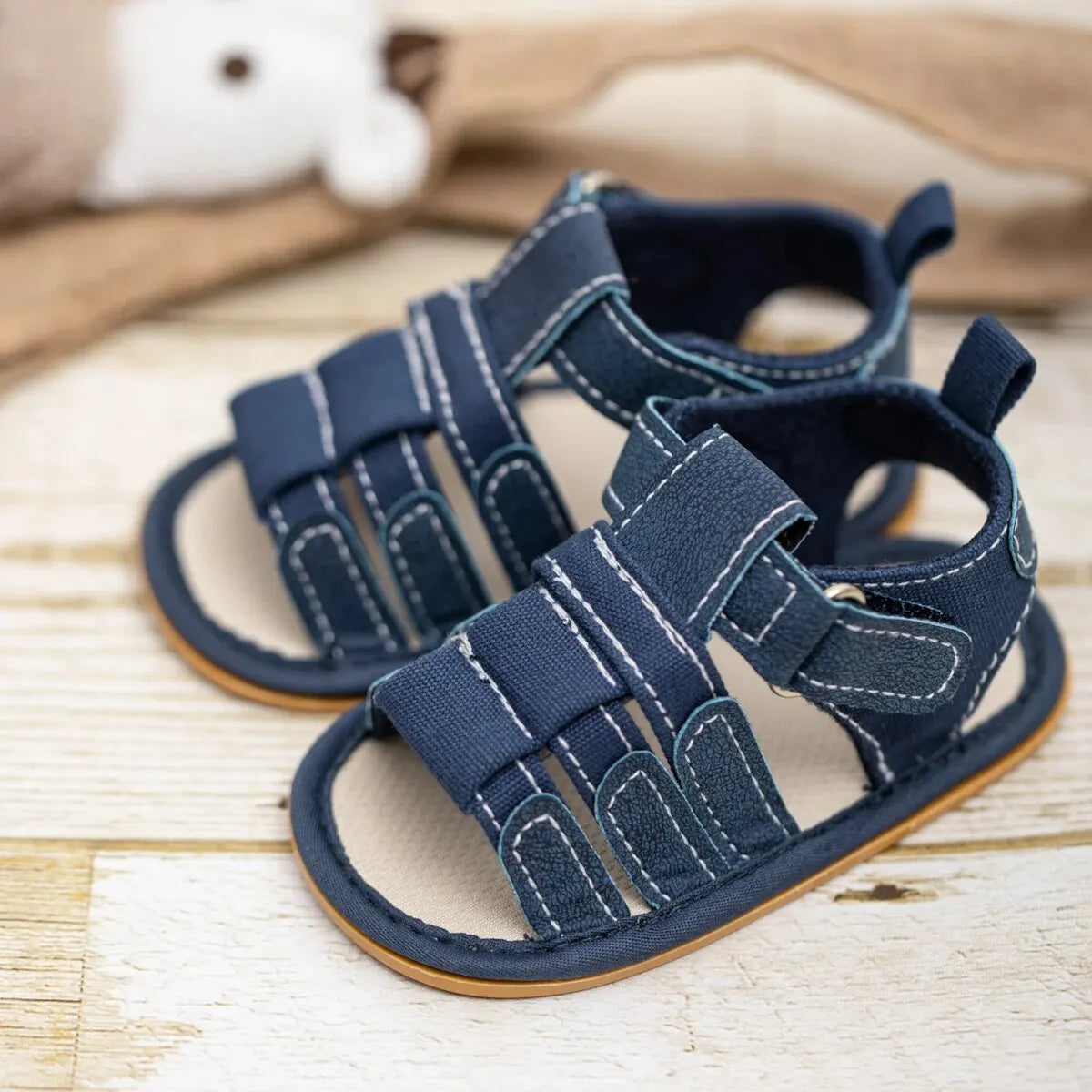 A pair of navy blue soft non-slip baby sandals for first walkers resting on a light wooden surface.