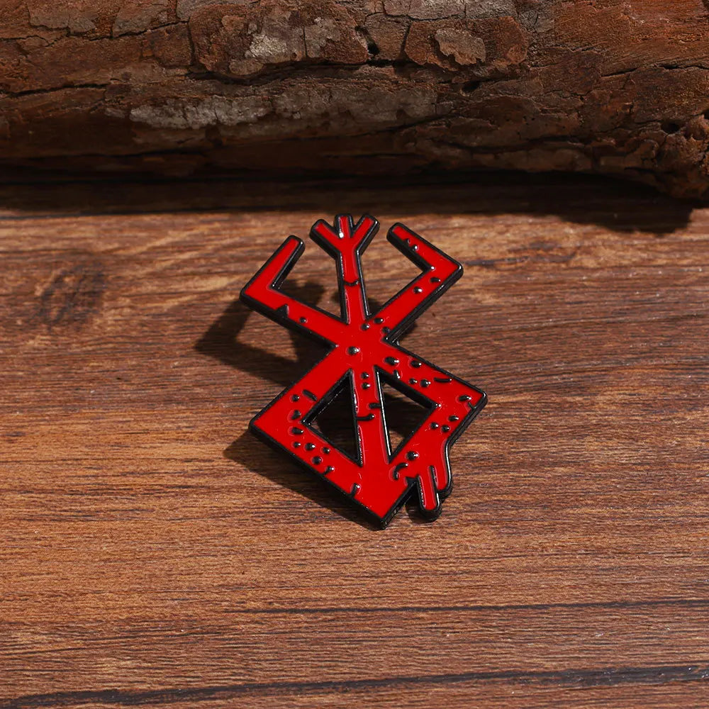 A red enamel lapel pin shaped like a stylized 'X' or cross, resting on a wooden surface.