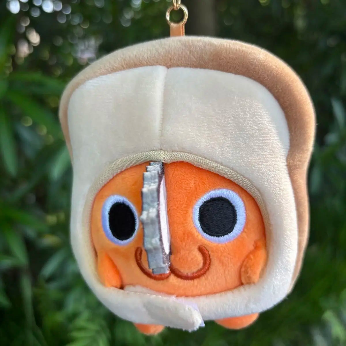 A soft orange plush doll with a white hood and a silver chainsaw blade detail, hanging from a gold-colored keychain.