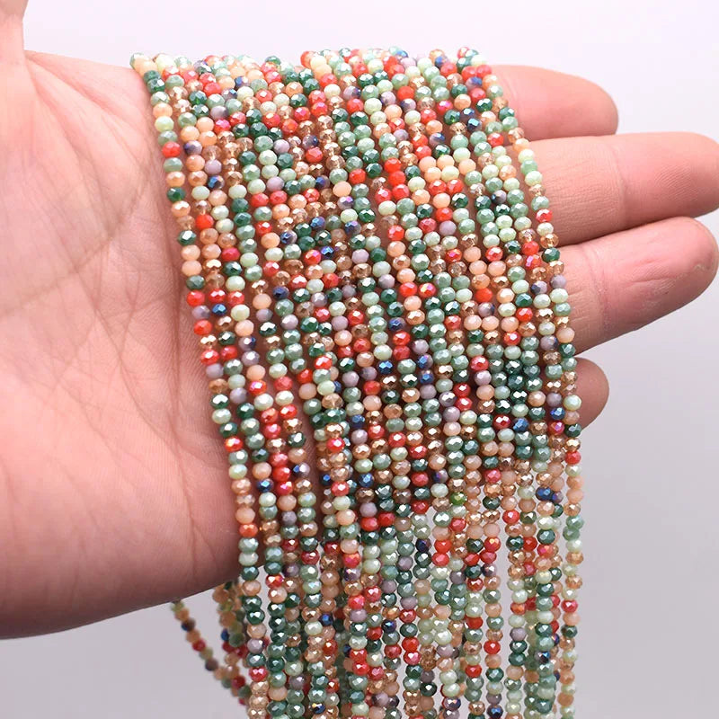A hand holds a strand of multicolored faceted crystal rondelle beads for jewelry making.