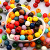 A bowl filled with various natural wooden beads in a wide assortment of colors including red, yellow, green, blue, and brown.