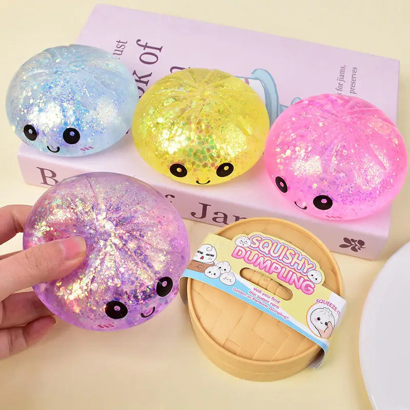 A hand holds a pink glitter squishy dumpling toy next to a box of similar toys.