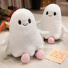 A white ghost plush toy with black eyes and pink feet is lying on a light surface.