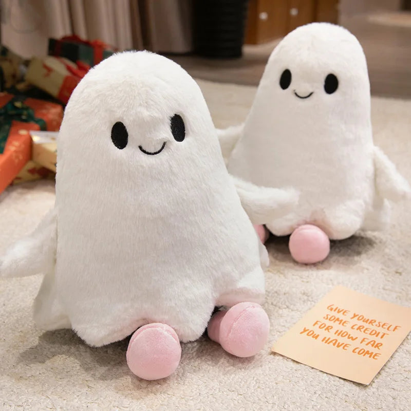 A white ghost plush toy with black eyes and pink feet is lying on a light surface.