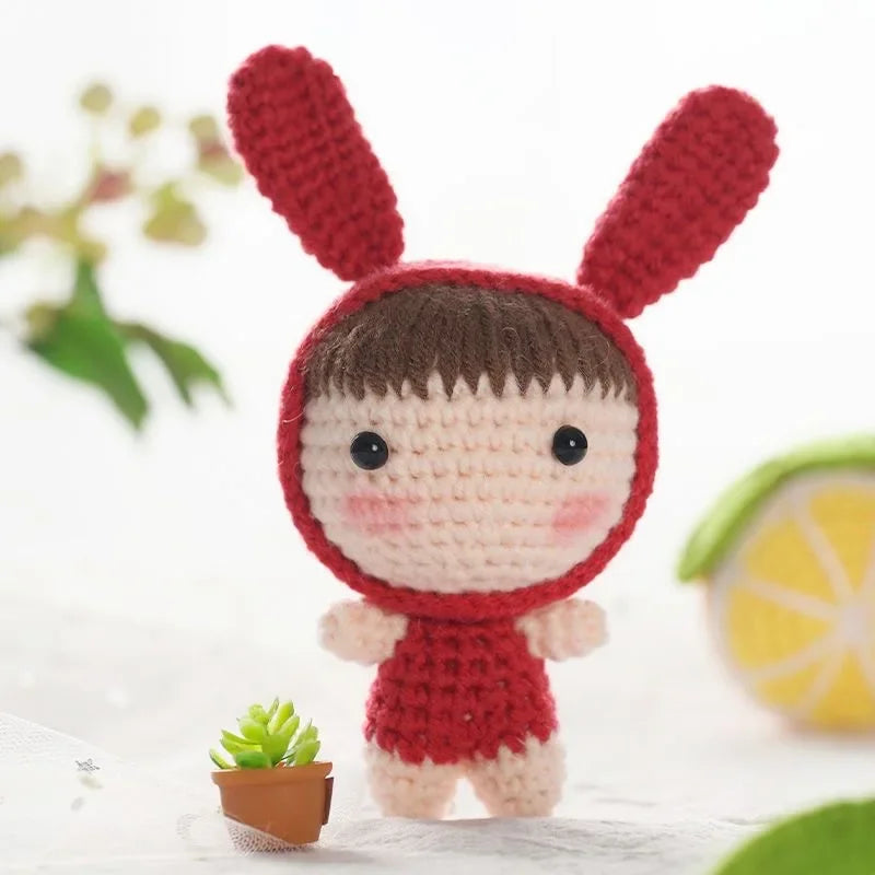 A handmade crochet doll kit featuring a red body and ears with brown hair, displayed on a white surface.