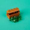 An orange building block treasure chest is open, revealing green gemstone-like pieces on a teal background.
