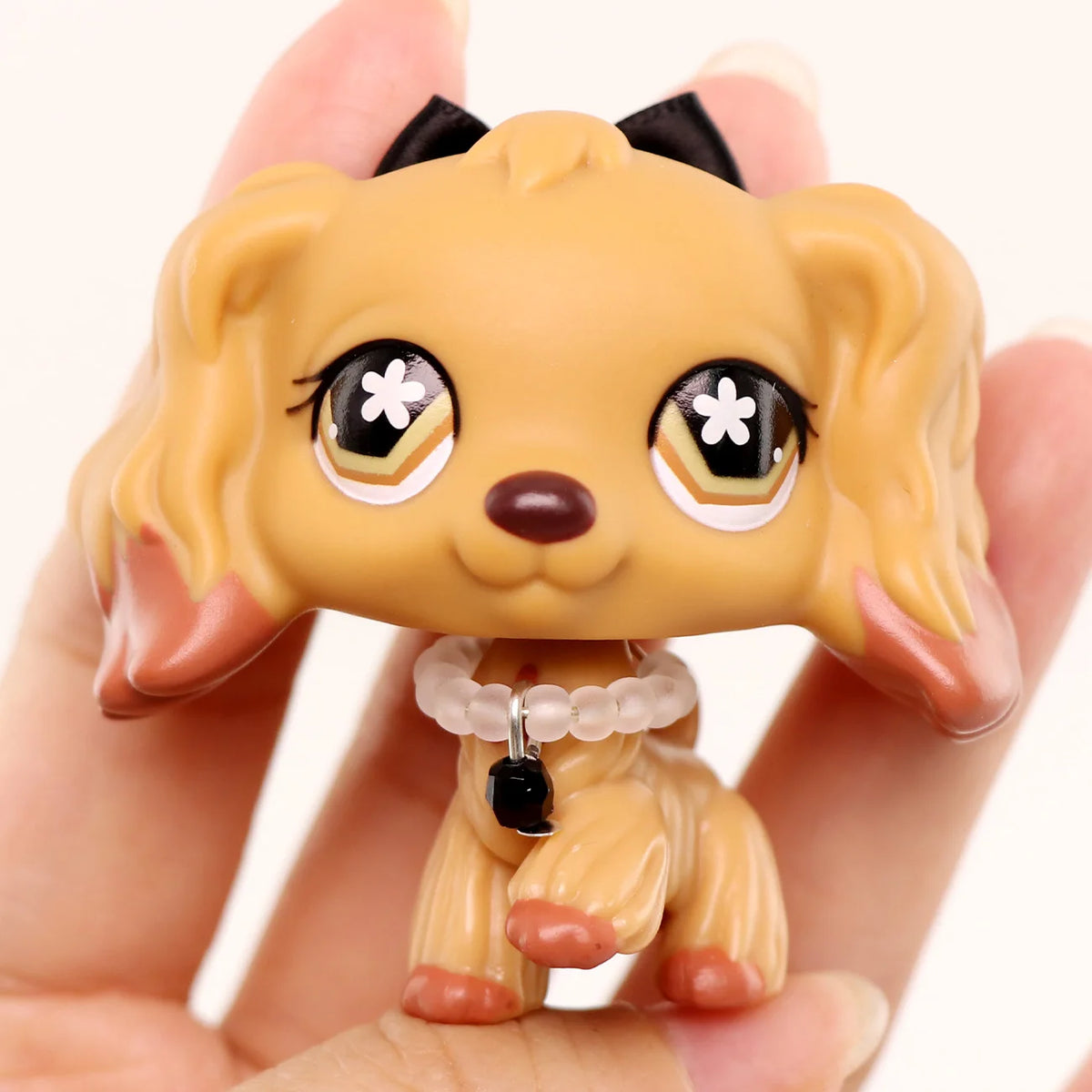 A small, light tan miniature pet animal figure with floppy ears and a collar is held in a person's hand.
