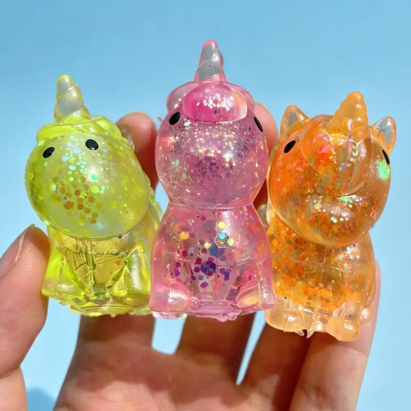 Drei glitzernde Einhorn-Stressbälle in Gelb, Pink und Orange werden in einer Hand gehalten.