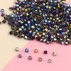 A pile of iridescent crystal glass beads in various sizes and colors, including purple, blue, gold, and black, scattered on a
