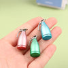 Three miniature alloy kettles in pink, teal, and green are held in a hand.