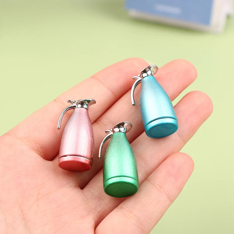 Three miniature alloy kettles in pink, teal, and green are held in a hand.