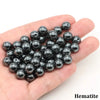 A handful of black hematite round beads is held in a person's hand.