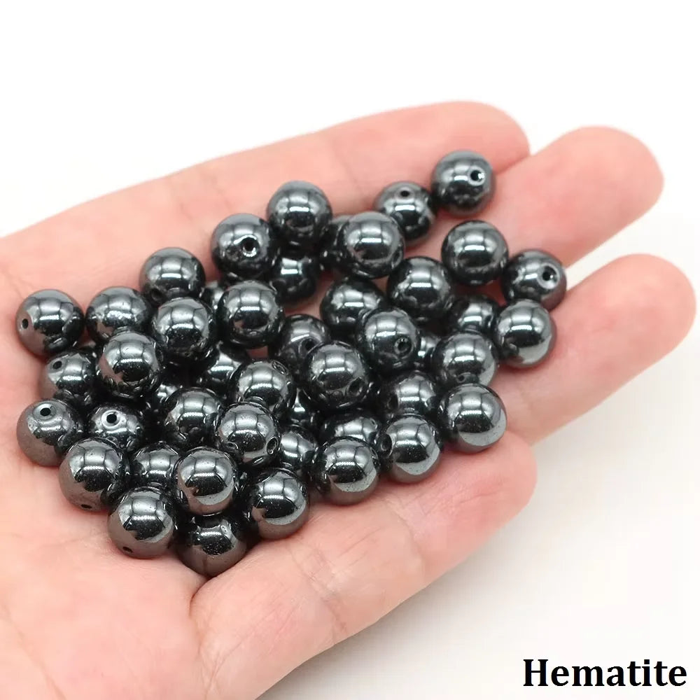 A handful of black hematite round beads is held in a person's hand.