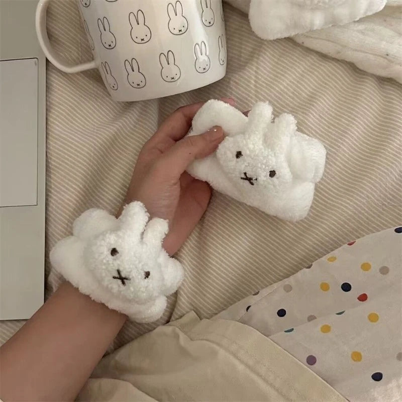 A hand is holding a white rabbit-shaped waterproof face wiping wristband on a light beige fabric.