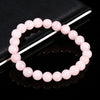 A bracelet made of small, round, natural pink quartz beads is displayed on a dark surface.