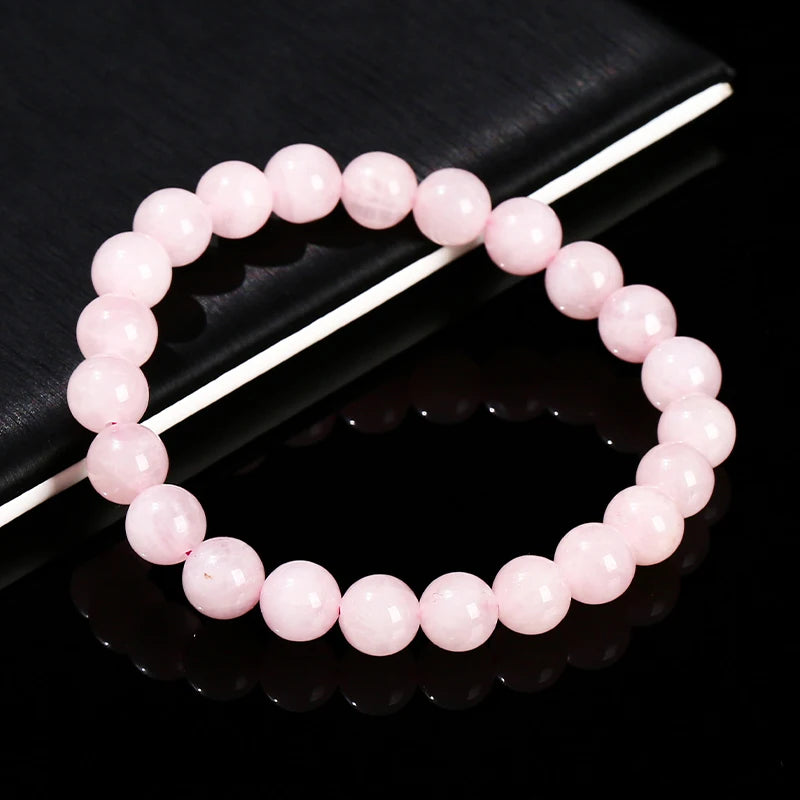 A bracelet made of small, round, natural pink quartz beads is displayed on a dark surface.