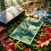 A green oracle card featuring a white lotus flower and crescent moon, resting on moss and autumn leaves.
