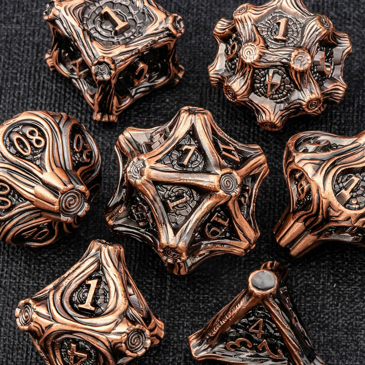 A collection of antique bronze and copper-toned metal dice, including a d10, arranged on a dark background.