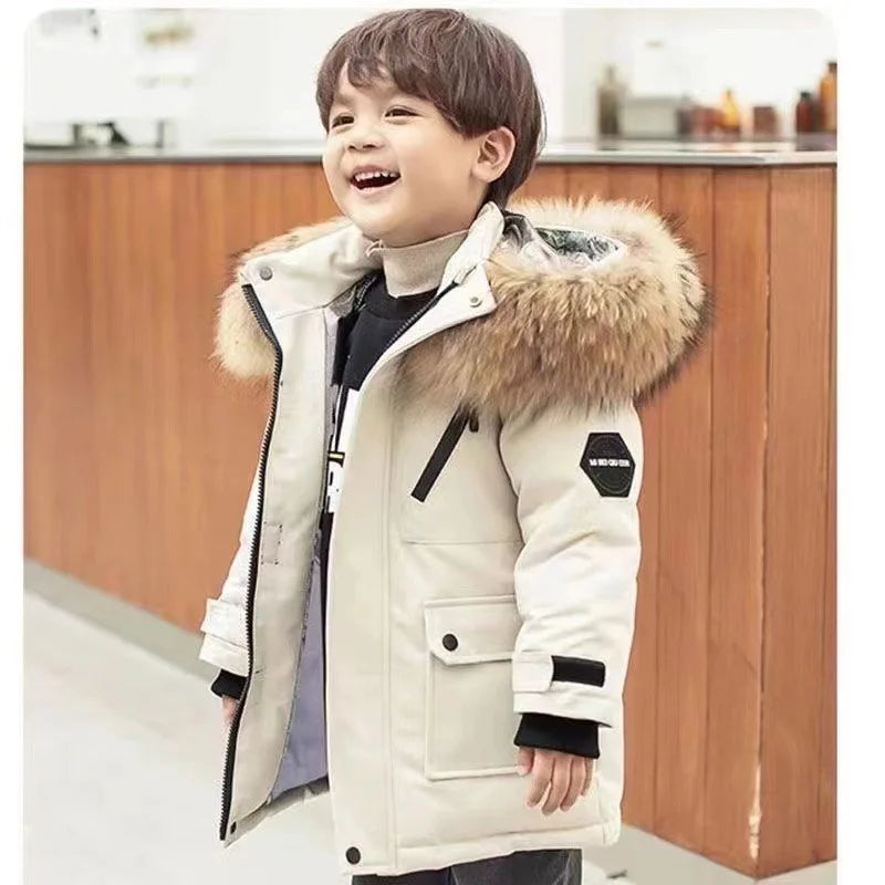 A young boy wearing a beige hooded winter jacket with a fluffy brown collar and black accents.