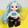A light blue articulated doll with long hair wearing a white shirt and patterned pants, displayed on a yellow fabric.