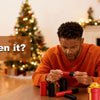 A man is opening a red nested screw gift box in a living room setting.