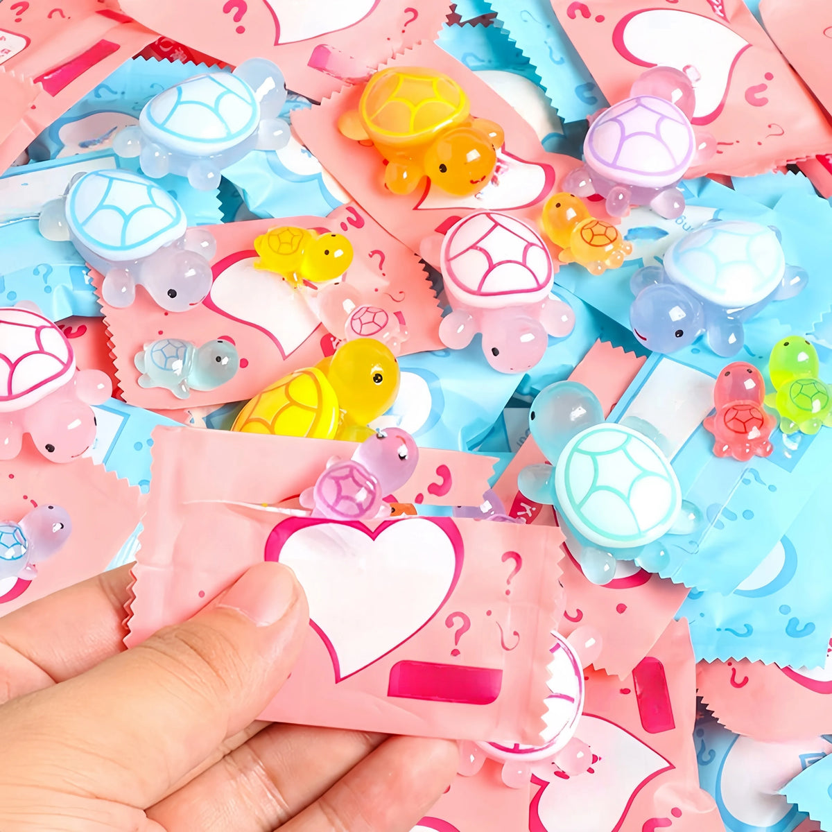 A hand holds a pile of glow in the dark mini turtle collectible figurines blind bags in various pastel colors.