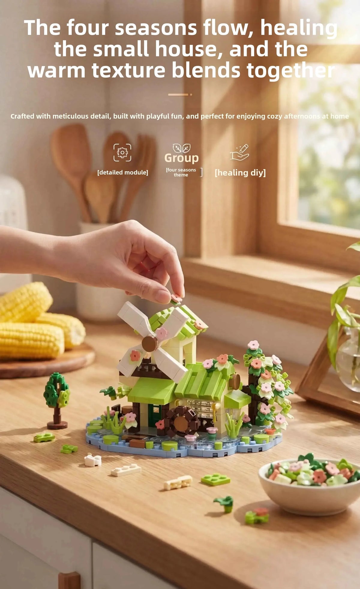 A hand places a miniature woodland cabin and windmill building set on a wooden surface with greenery.